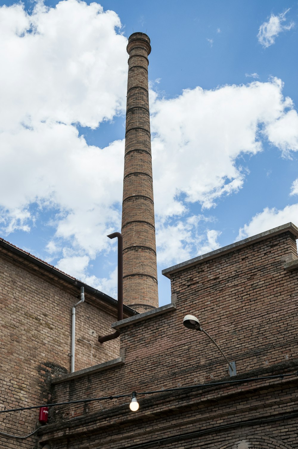 a brick building with a tall chimney in front of a cloudy blue sky