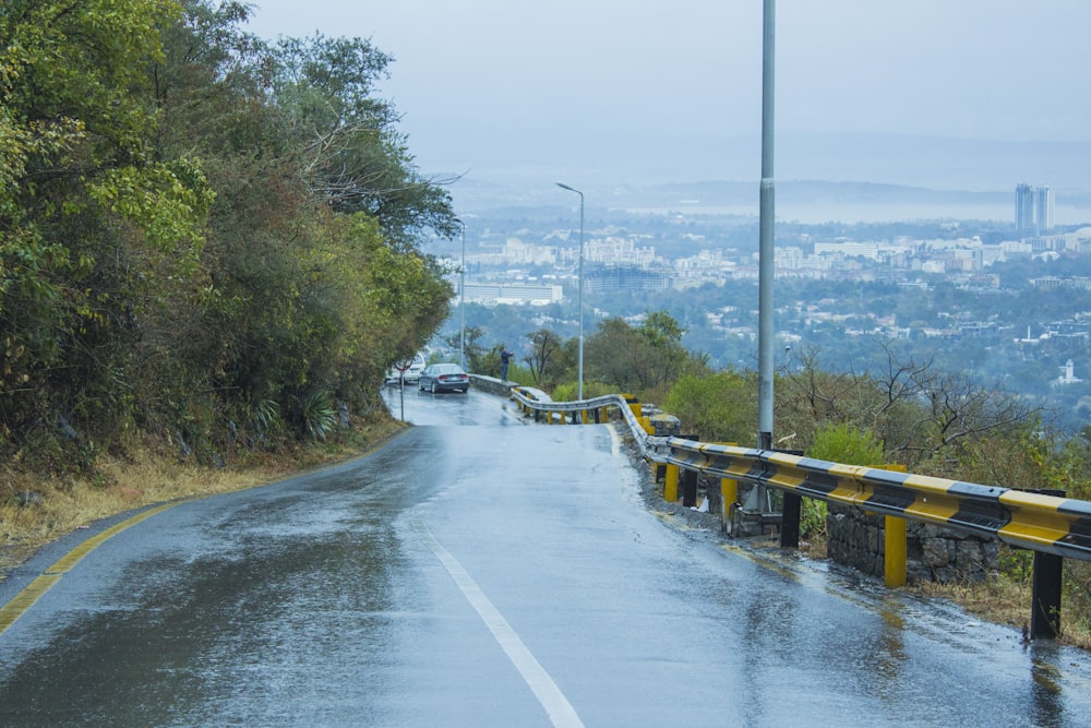 a wet road with a yellow guard rail on the side