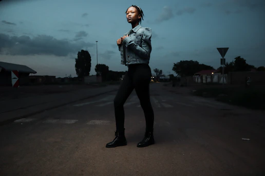 A stylish man wearing a sleek jacket and jeans, standing confidently on a city street at dusk.