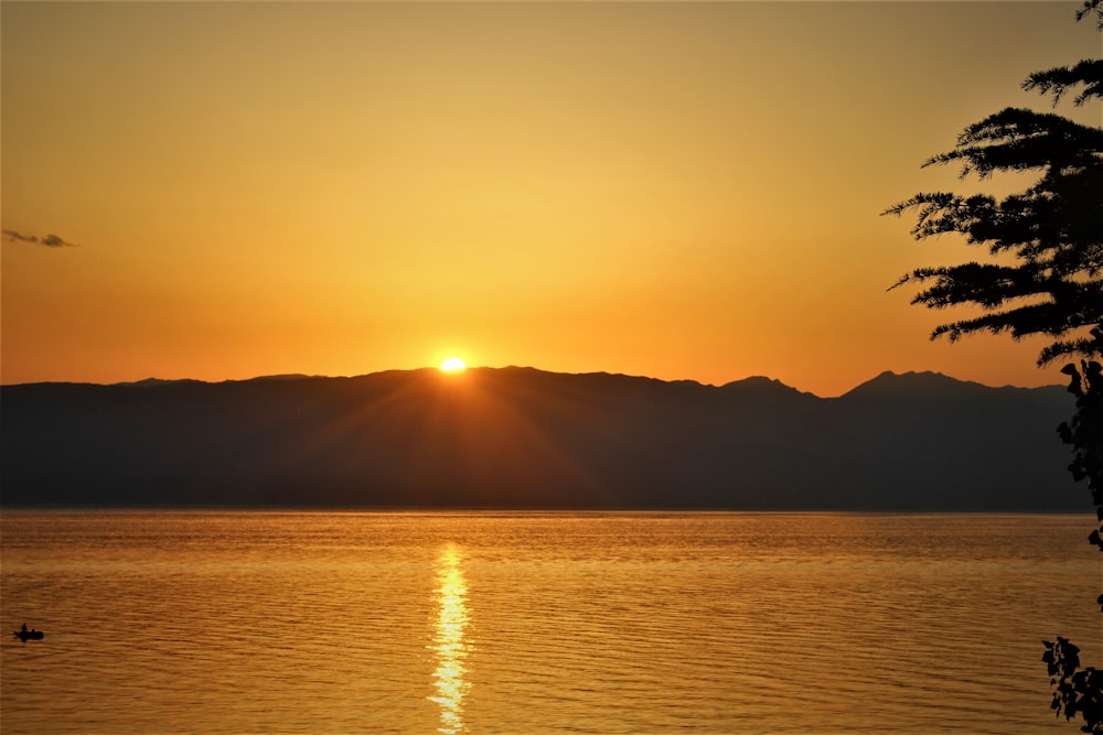 the sun is setting over a lake with mountains in the background