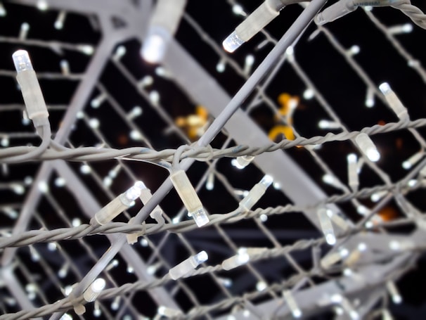 Numerous white LED string lights are intertwined, creating a lattice pattern against a dark background. The lights are arranged closely together, with each bulb emitting a bright, white glow.