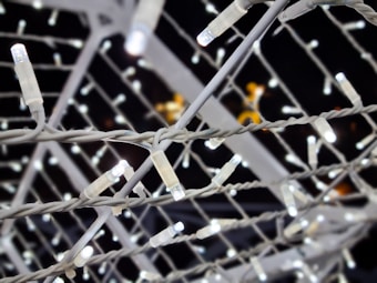 Numerous white LED string lights are intertwined, creating a lattice pattern against a dark background. The lights are arranged closely together, with each bulb emitting a bright, white glow.