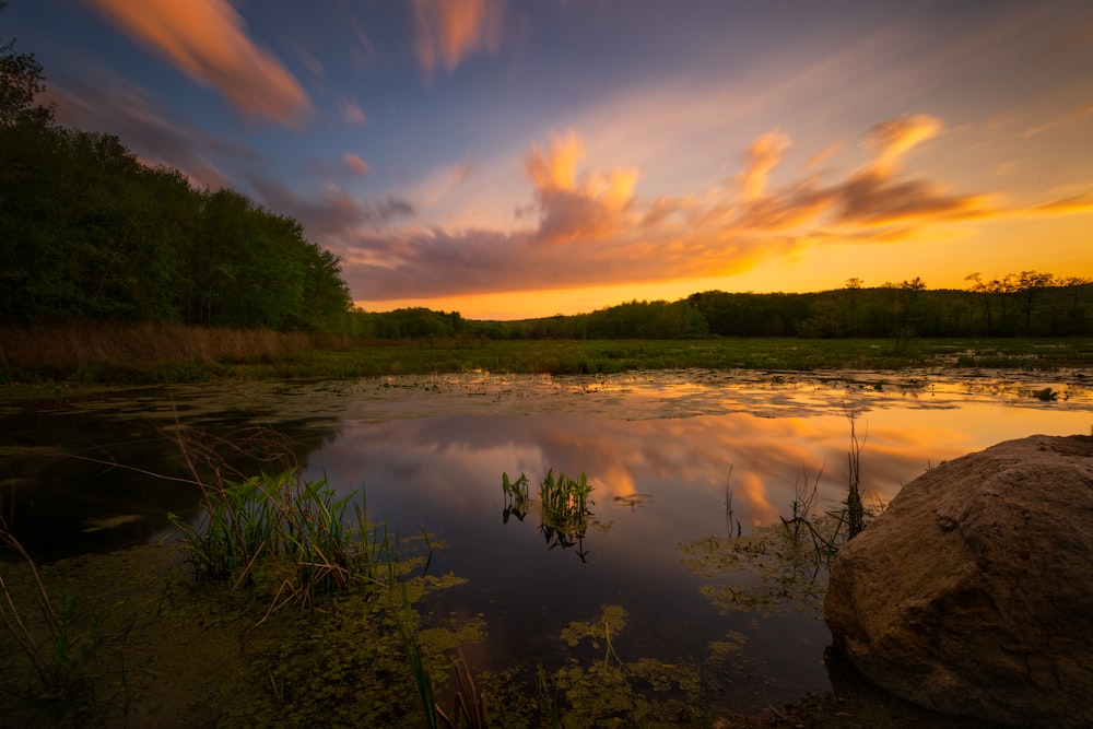 a sunset over a pond with a rock in the foreground