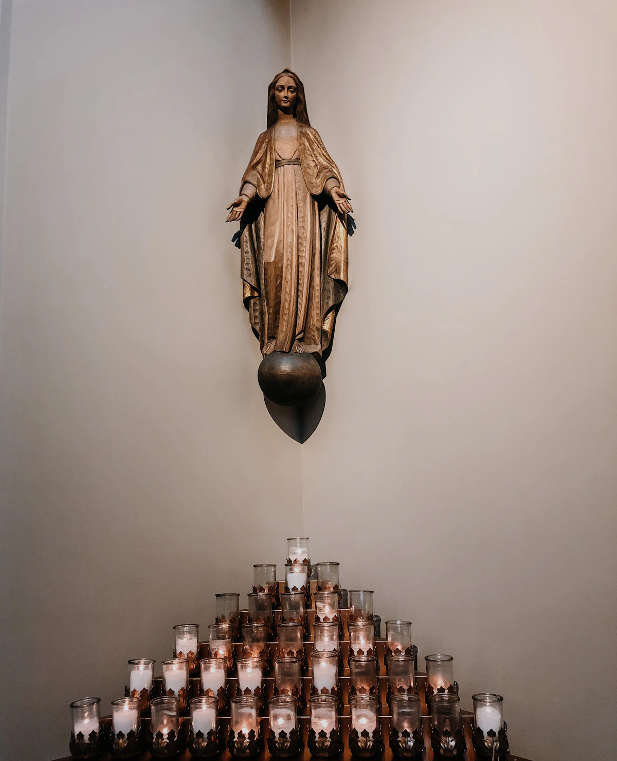 A golden statue of the Virgin Mary above a pyramid of votive candles