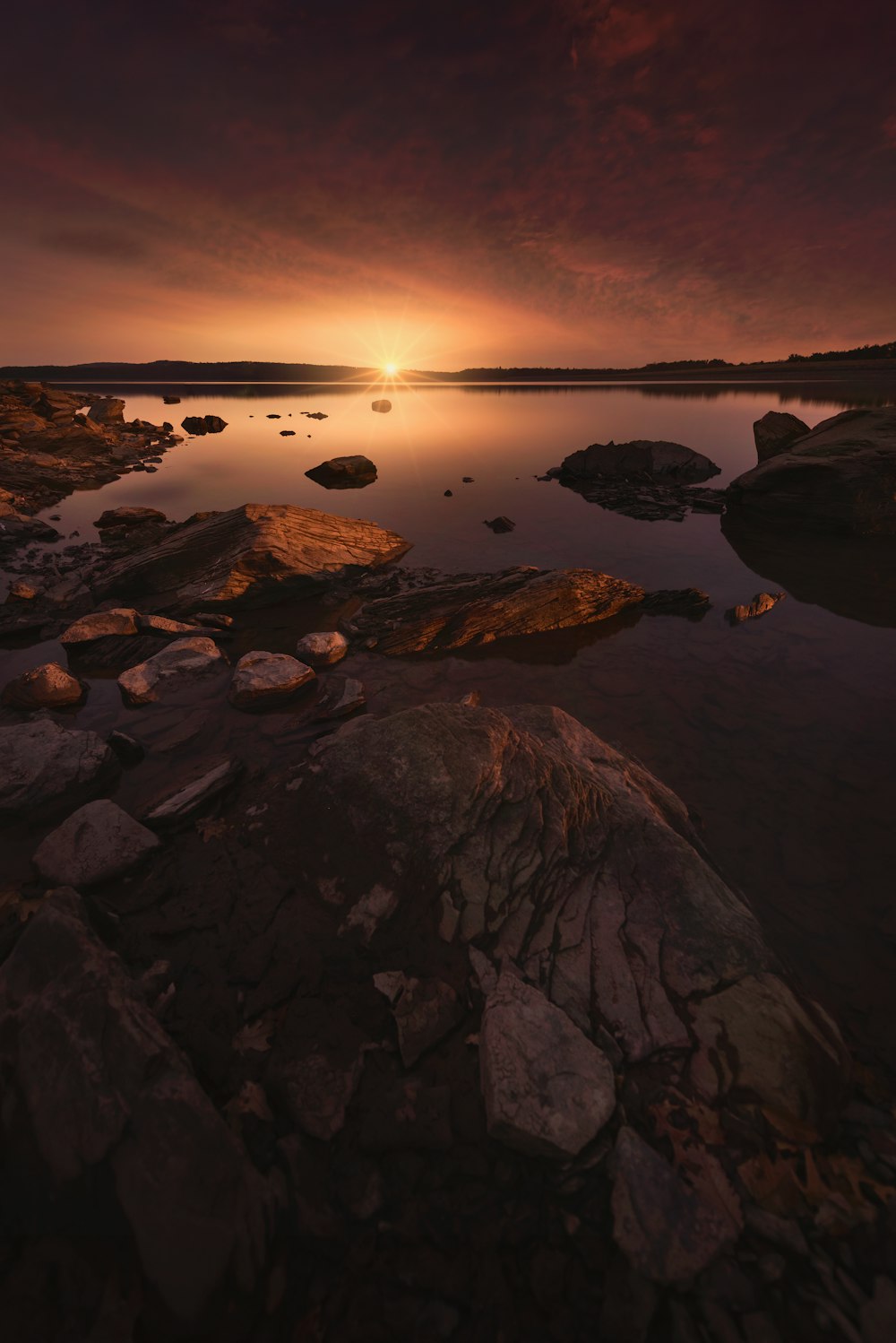 a sunset over a body of water with rocks in the foreground