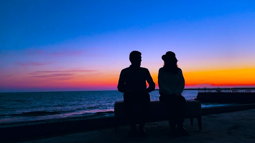 a man and a woman sitting on a bench watching the sunset