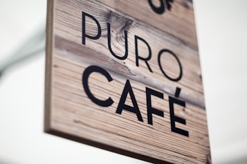A wooden sign displaying the text 'PURO CAF&Eacute;' with a rustic, natural appearance. The background is a light wood texture with visible grains, and the font is bold in black.