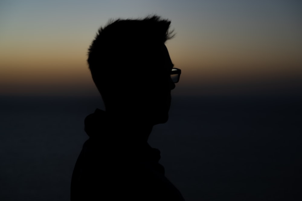 a silhouette of a man with glasses in front of a sunset