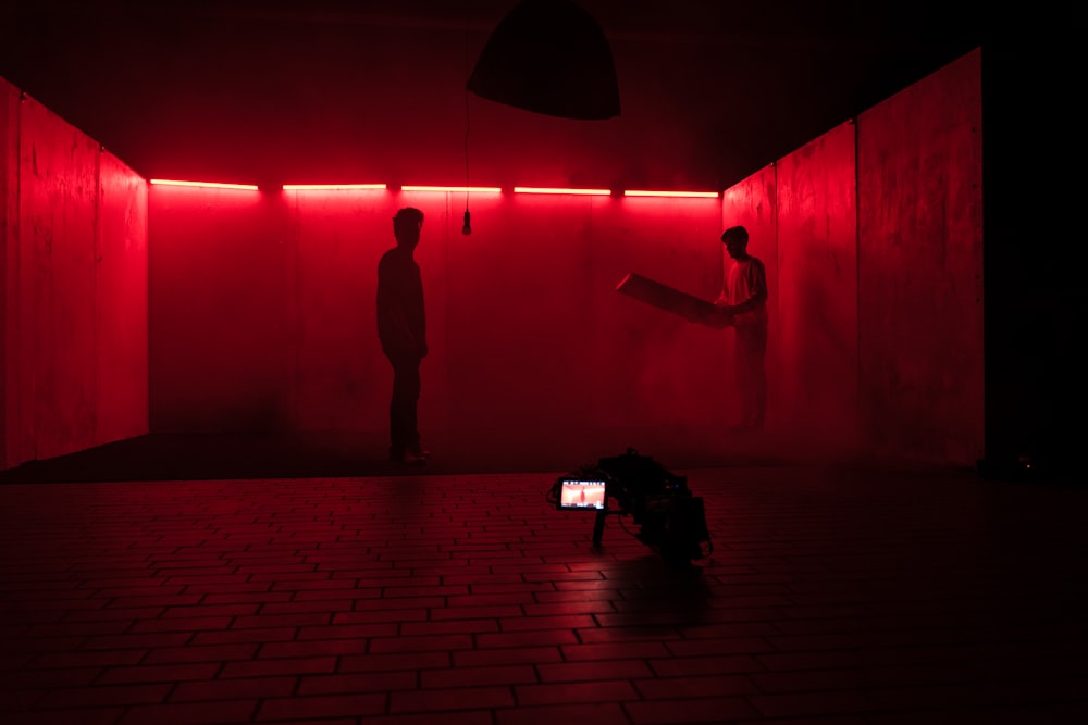 two people standing in a dark room with a red light