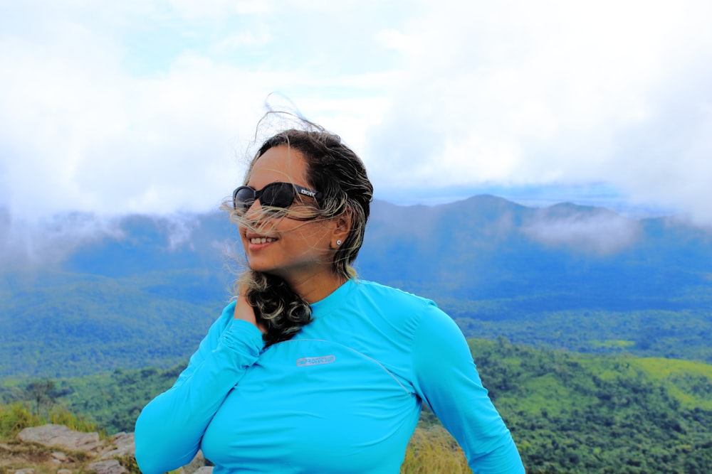 a woman in a blue shirt is standing on a mountain