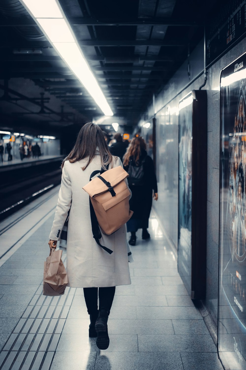 a woman with a backpack walks down a subway platform