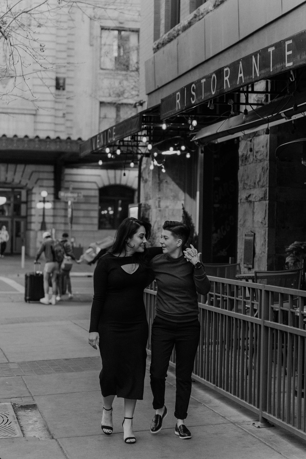 two women walking down a sidewalk in front of a store