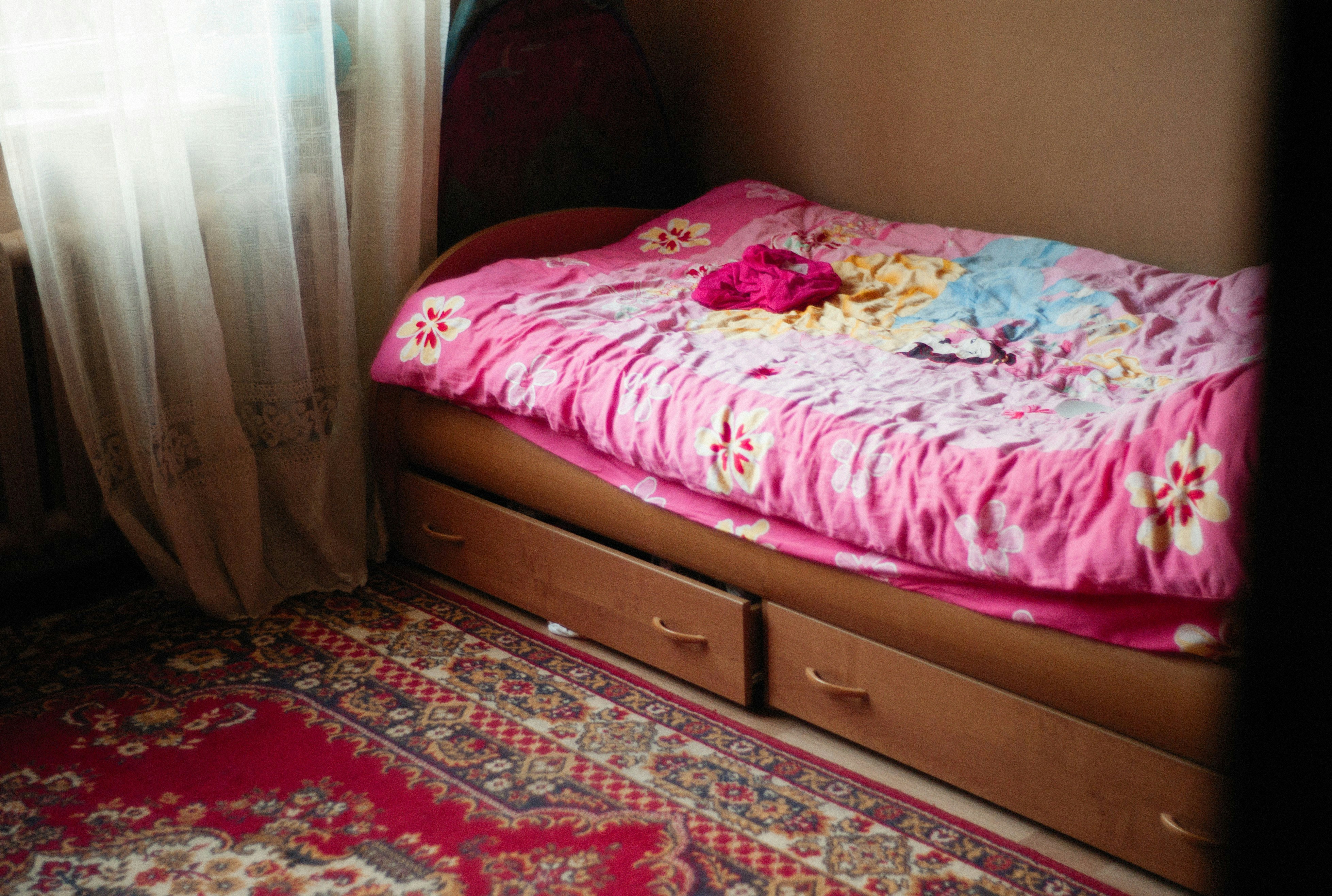 A small bed with a pink blanket on top of it