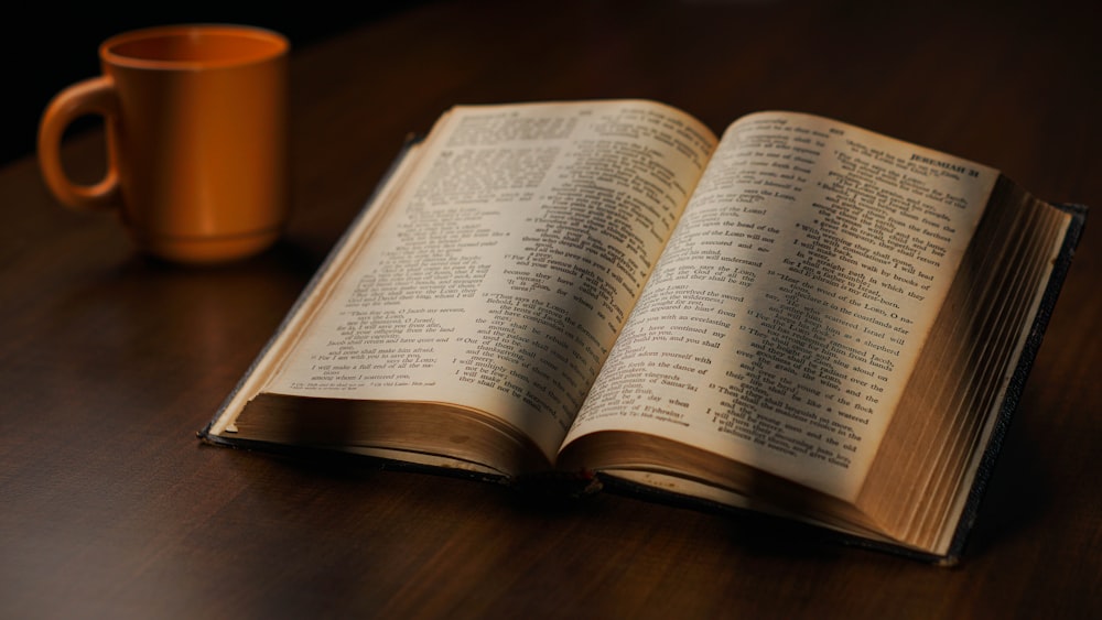 an open book sitting on top of a wooden table next to a cup