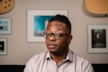 a man with glasses sitting in front of a wall
