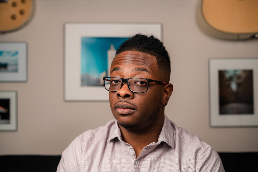 a man with glasses sitting in front of a wall