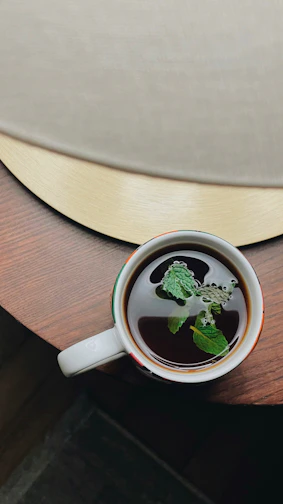 Steaming cup of abanoz tea on a wooden table with fresh tea leaves nearby.