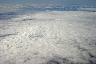 A vast expanse of clouds seen from above, with a dense, textured blanket that stretches into the horizon. The lighting creates subtle shadows and highlights on the cloud surface.