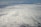 A vast expanse of clouds seen from above, with a dense, textured blanket that stretches into the horizon. The lighting creates subtle shadows and highlights on the cloud surface.