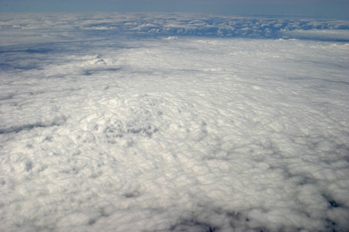 A vast expanse of clouds seen from above, with a dense, textured blanket that stretches into the horizon. The lighting creates subtle shadows and highlights on the cloud surface.