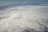 A vast expanse of clouds seen from above, with a dense, textured blanket that stretches into the horizon. The lighting creates subtle shadows and highlights on the cloud surface.
