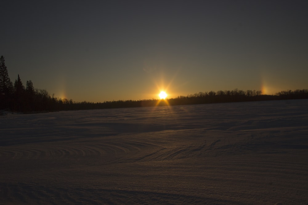 the sun is setting over a snowy field