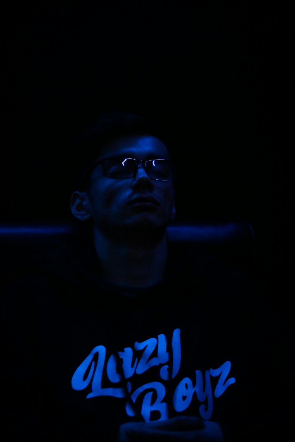 a man with glasses sitting in the dark