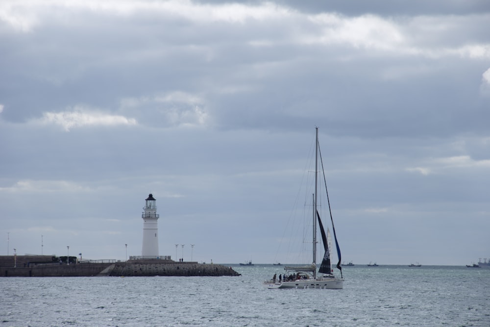 a sailboat in the water with a lighthouse in the background