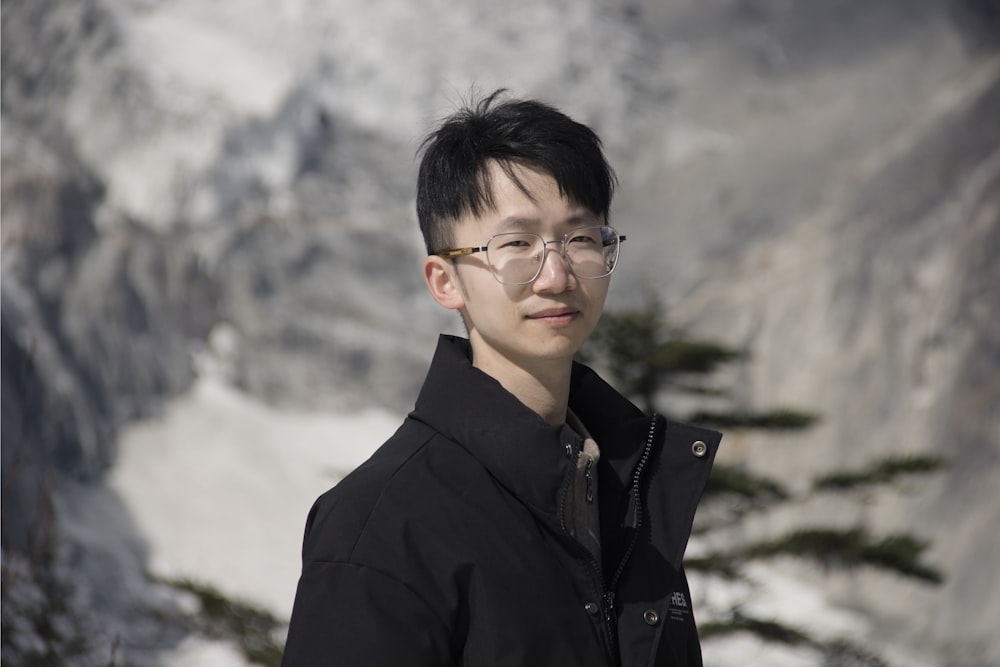 a man wearing glasses standing in front of a mountain