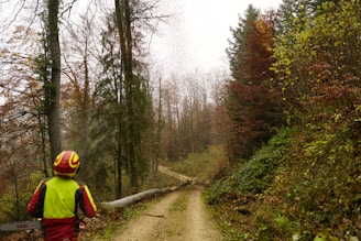 a man walking down a dirt road next to a forest