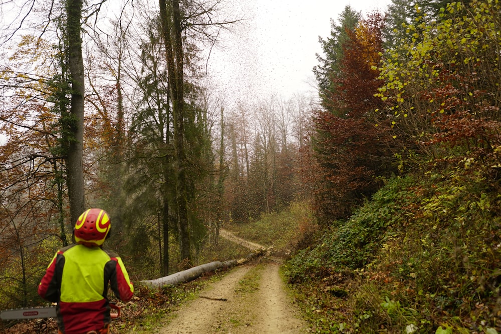 a man walking down a dirt road next to a forest