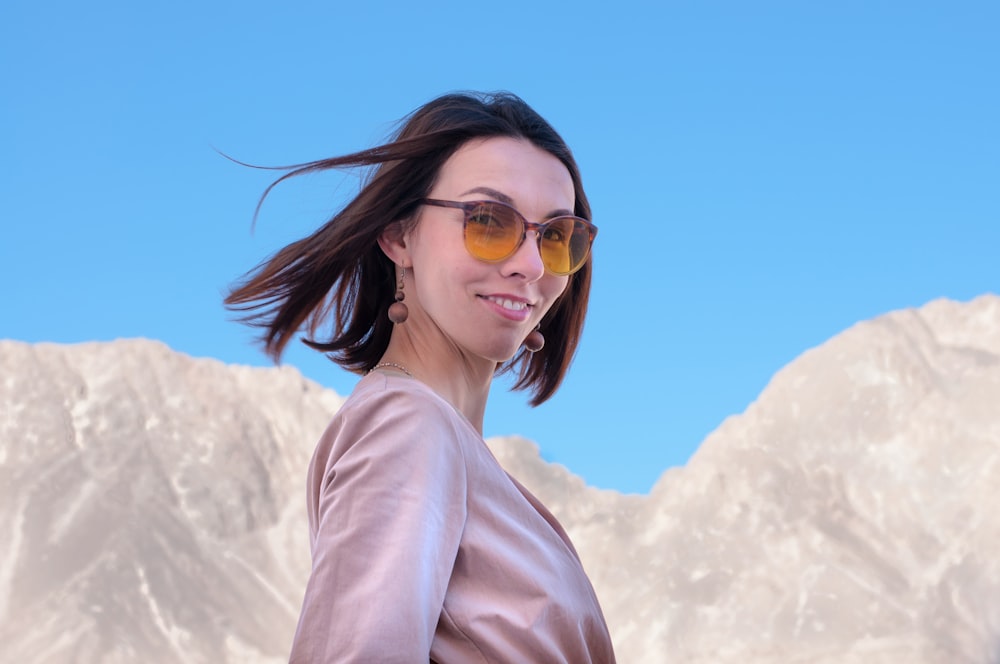 a woman wearing sunglasses standing in front of a mountain