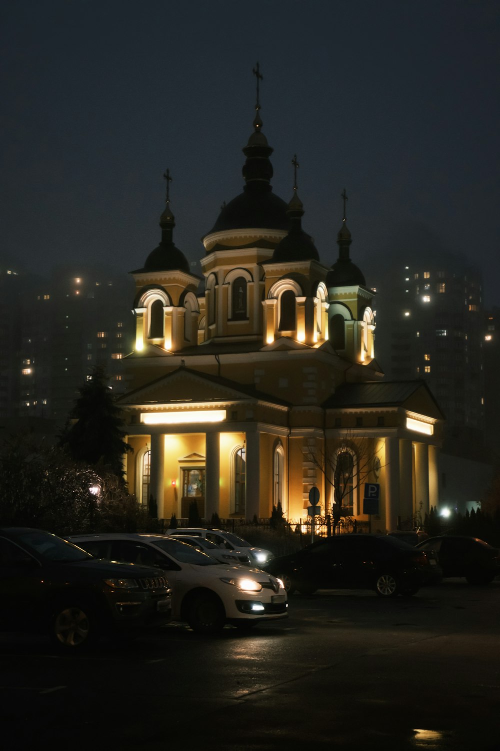 a church lit up at night with cars parked in front of it