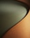 A close-up view of a piece of furniture with a textured, ribbed fabric surface in a warm, earthy brown color, forming a smooth, gently curving shape. The seat cushion is upholstered in a solid, muted green fabric, providing a contrasting texture and color.