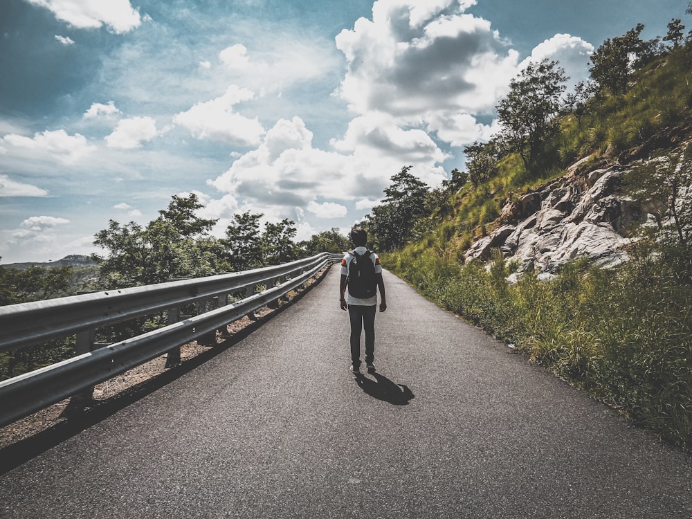 a man walking down a road next to a lush green hillside