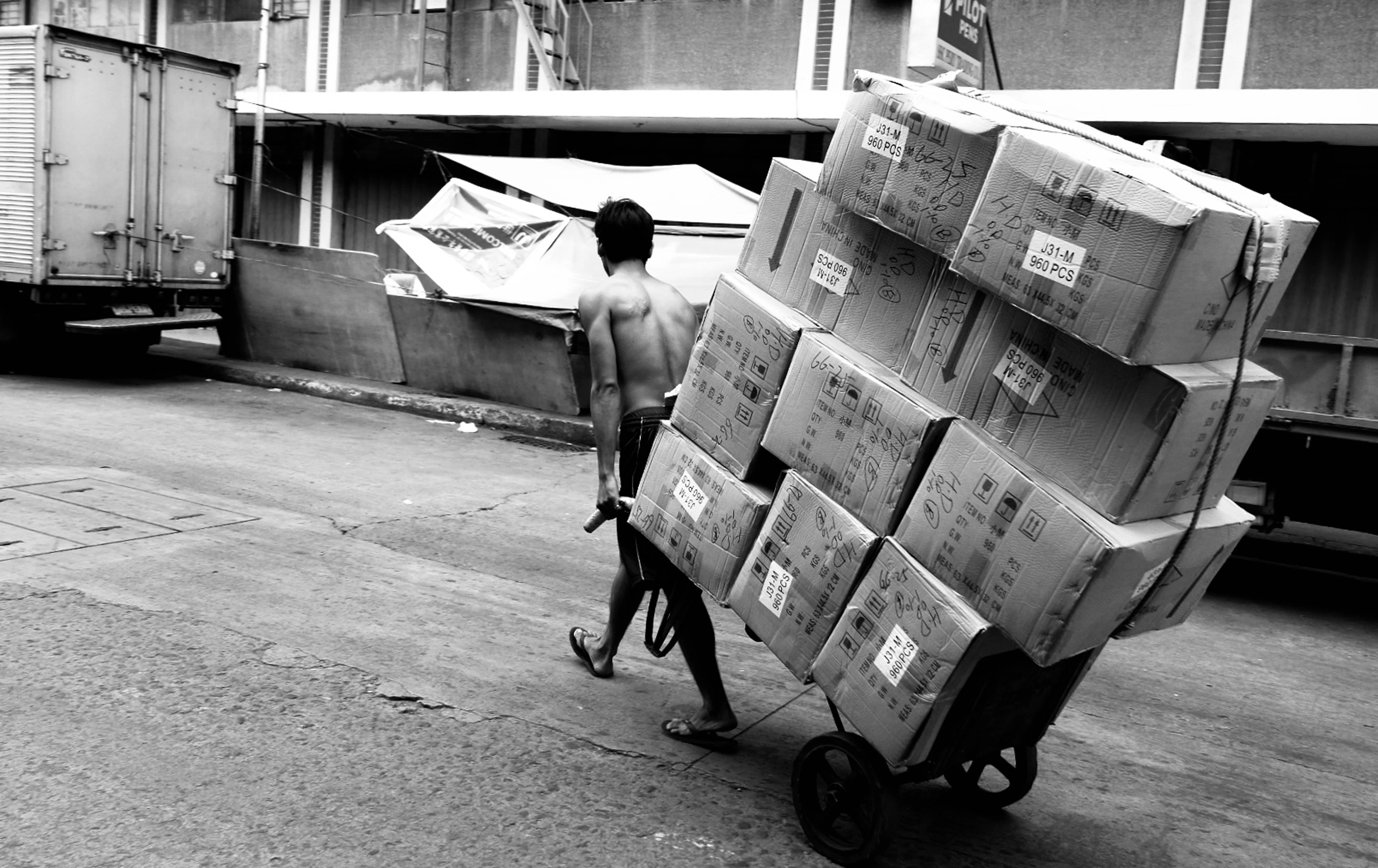 Labourer pushing a hand cart piled with cartons down a street