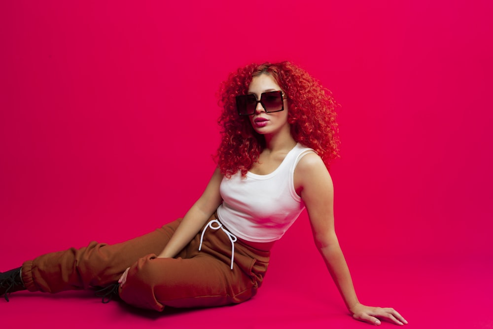 a woman with red hair and sunglasses sitting on the ground