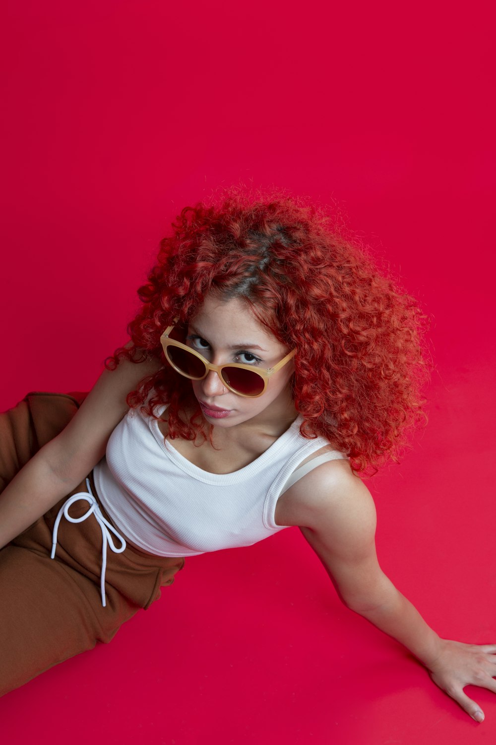 a woman with red hair and sunglasses on a pink background