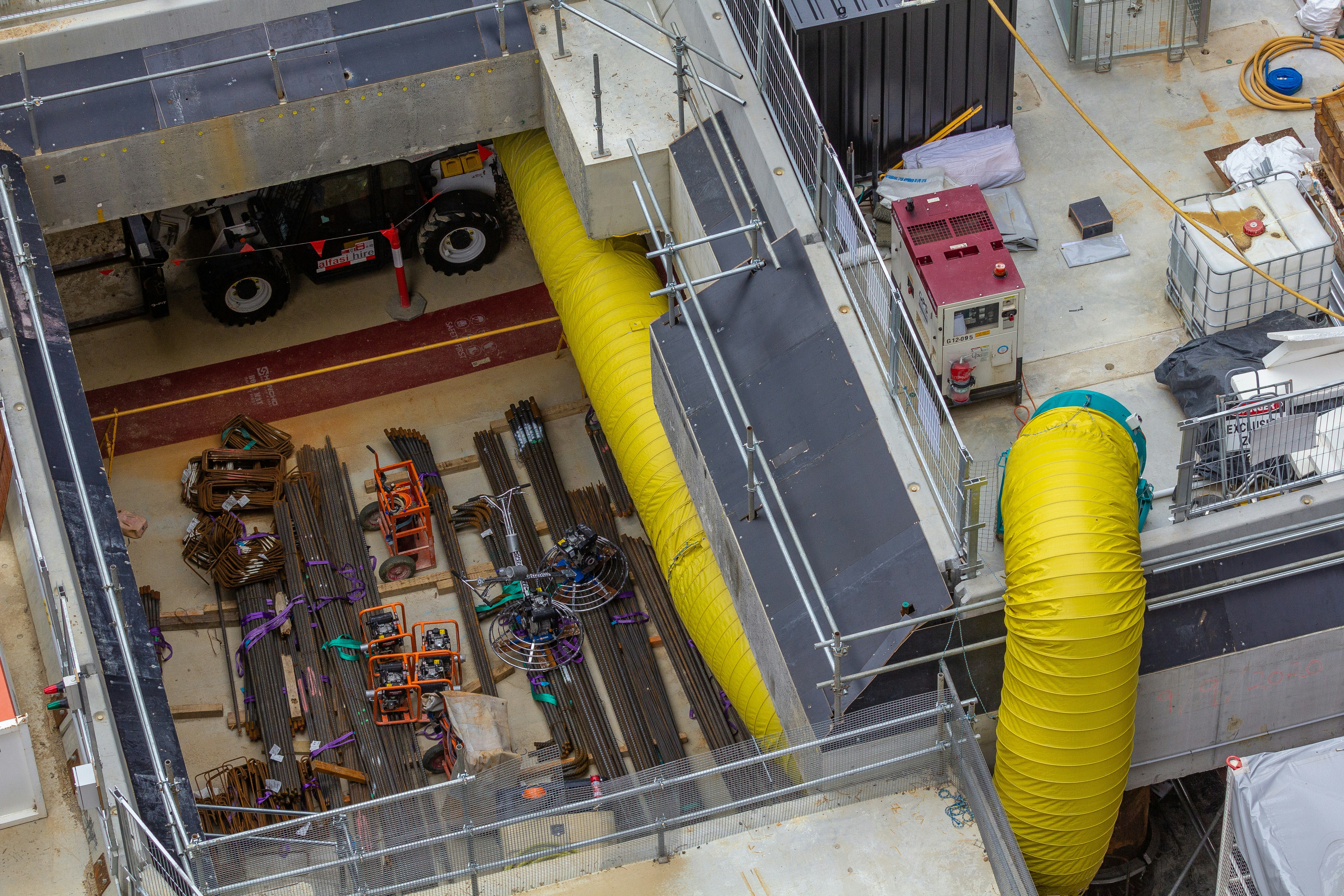 Civil construction site with concrete structures, scaffolding and rebar visible, bright daylight, workers in safety gear