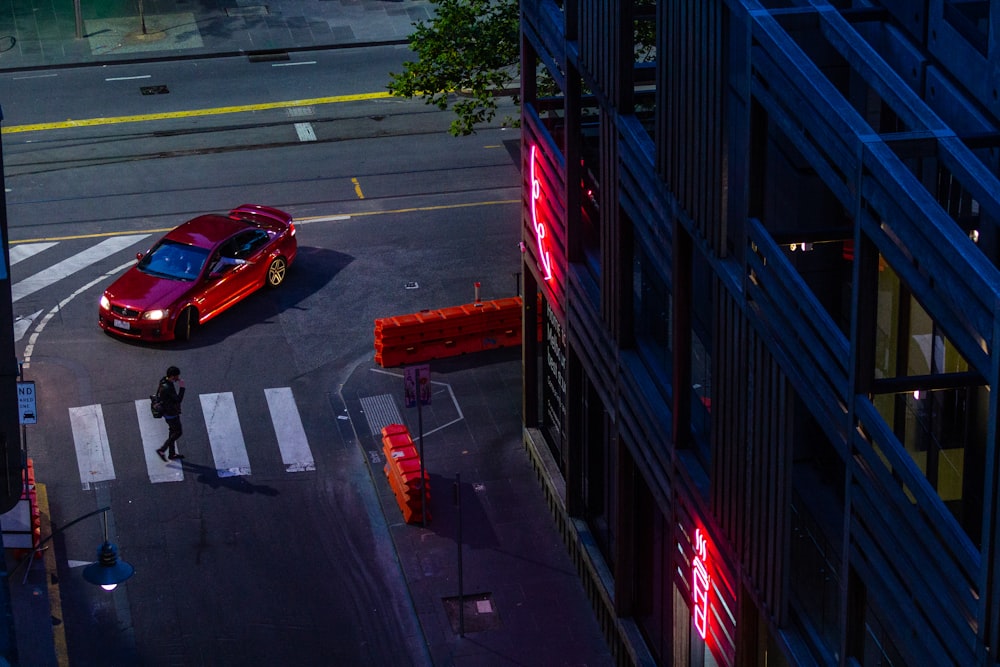 a red car driving down a street next to a tall building