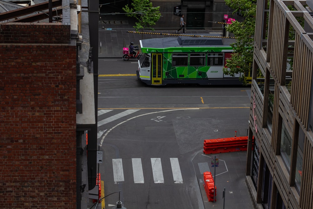 a green bus driving down a street next to tall buildings