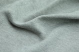 A close-up view of soft, ribbed fabric with a light green hue. The texture is detailed, revealing the individual knitting patterns with slight shadows and highlights, suggesting gentle folds and a smooth surface.