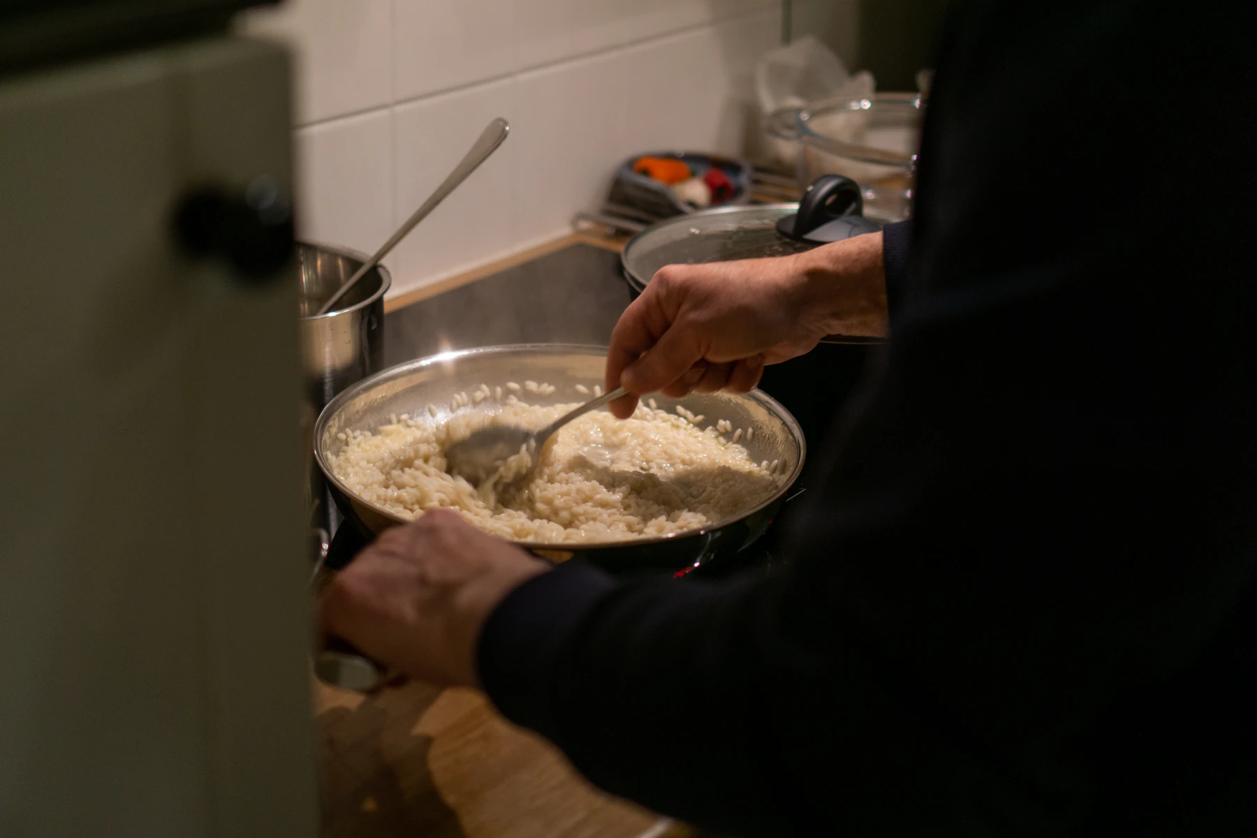 A home cook stirring risotto in a wide steel pan on the stove