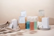 A minimalist arrangement of eco-friendly cleaning products including various bottles, containers, and packaging. The items are neatly placed on a soft beige fabric backdrop, emphasizing a sustainable and natural aesthetic.