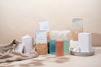 A minimalist arrangement of eco-friendly cleaning products including various bottles, containers, and packaging. The items are neatly placed on a soft beige fabric backdrop, emphasizing a sustainable and natural aesthetic.