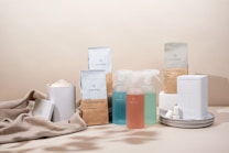 A minimalist arrangement of eco-friendly cleaning products including various bottles, containers, and packaging. The items are neatly placed on a soft beige fabric backdrop, emphasizing a sustainable and natural aesthetic.