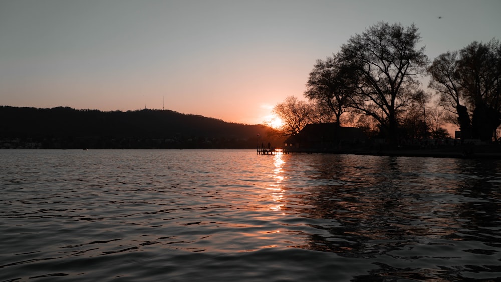 the sun is setting over a lake with trees