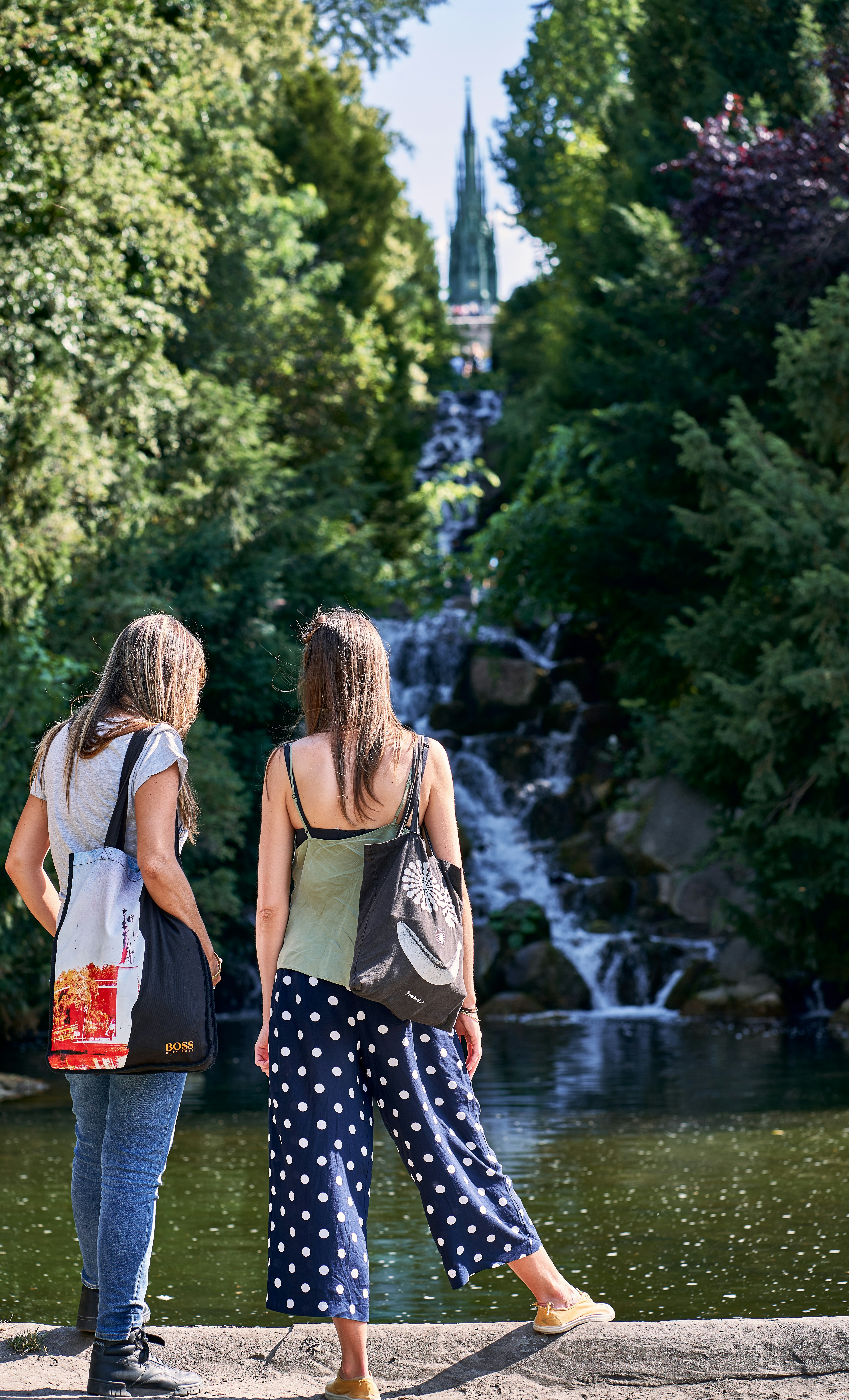 湖のほとりに立って滝を見ている2人の女性