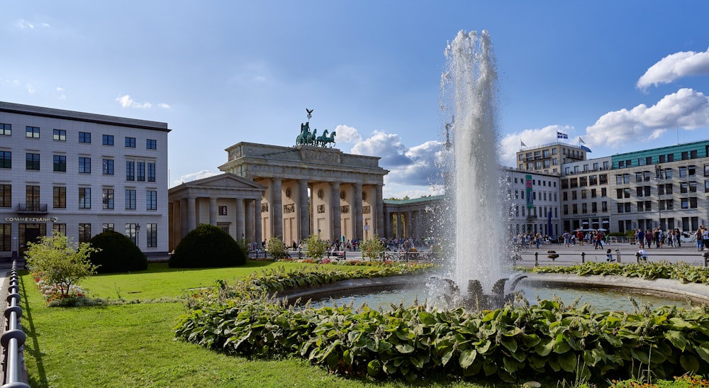 a fountain in the middle of a park with buildings in the background