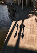 a group of people walking down a sidewalk next to a body of water